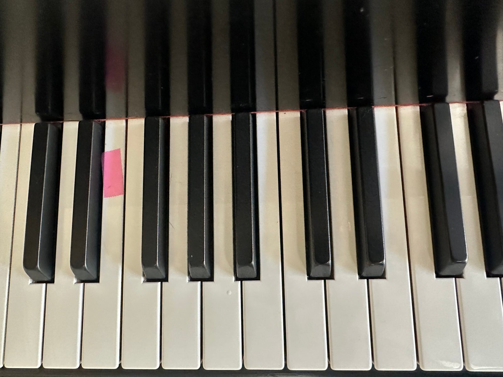 Piano keys seen from above with a pink sticky note marking a landing key